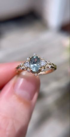 someone is holding an engagement ring with a blue stone in it's middle finger