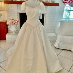 a white wedding dress is on display in front of a fire place with flowers around it