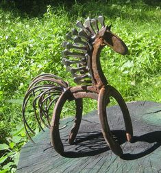 a metal horse sculpture sitting on top of a wooden table next to grass and bushes