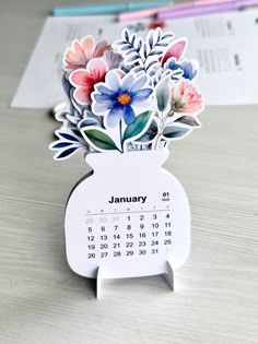 a desk calendar with flowers on it sitting on top of a table next to a pen and paper