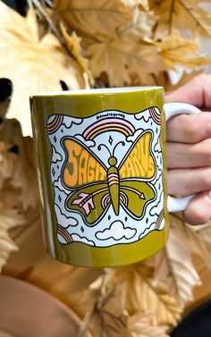 a person holding a coffee mug in front of some autumn leaves with the words sagit's on it