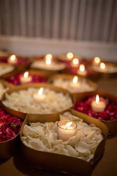 many candles are lit in small boxes filled with flowers and petals on a table top