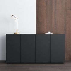 a black cabinet sitting next to a white lamp on top of a wooden floor in front of a wall