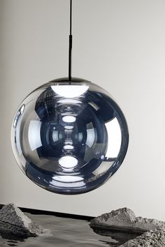 a large glass ball hanging from a ceiling light over rocks and water in a room with white walls