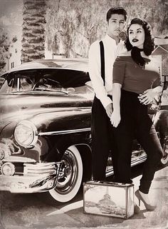 a man and woman standing next to an old car