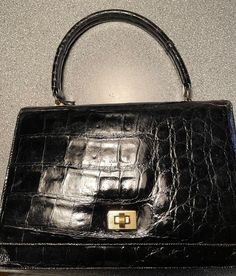 A 1950's style black alligator handbag. with a long flap closure and a rounded handle. Very neat, precise, and, what can I say, black alligator.  7"x9.5" from handle 11" total height   Priced way way below the designer bags, which aren't nearly as nice.   $570 Classic Crocodile Pattern Satchel, Vintage Business Bag With Crocodile Pattern, Vintage Business Bags With Crocodile Pattern, Vintage Crocodile Pattern Business Bag, Alligator Handbags, Black Alligator, Top Handle Bags, 1950s Fashion, Designer Bags