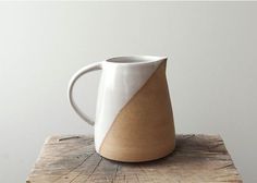 a white and brown coffee mug sitting on top of a wooden table next to a wall