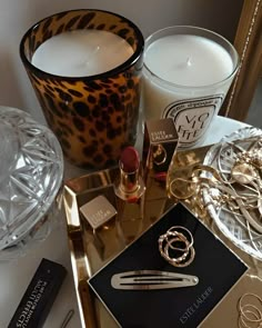 a table topped with candles and jewelry next to a glass container filled with lipsticks