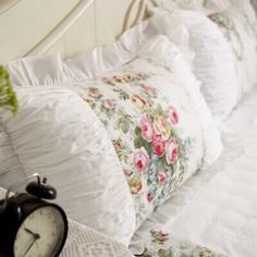 an alarm clock sitting on top of a white bed next to pillows and blankets in a room