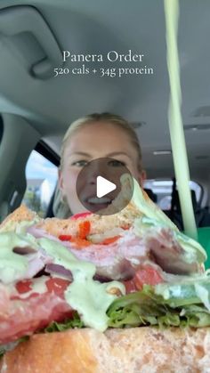 a woman sitting in the back seat of a car with a large sandwich on it