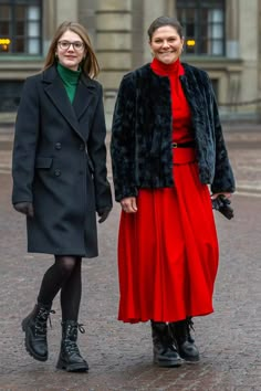 two women standing next to each other in front of a building wearing coats and boots