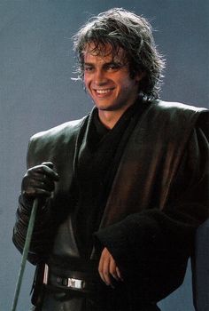 a man dressed as darth vader holding a green stick and smiling at the camera