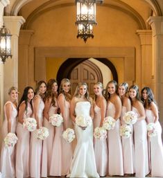 a group of women standing next to each other in front of a doorway holding bouquets