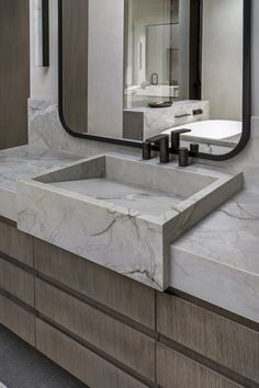 a bathroom with marble counter top and large mirror over it's sink, in front of a wall mounted faucet