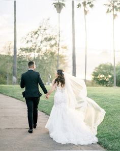 a bride and groom holding hands walking down a path with palm trees in the background