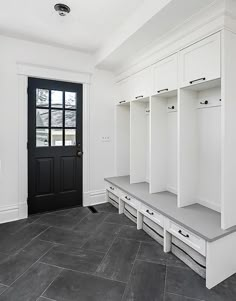 a black door and some white cabinets in a room with gray tile flooring on the walls