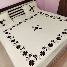 a white bed with black and red flowers on the comforter is in front of a pink wall