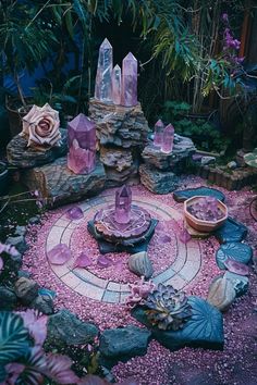 a garden filled with lots of purple rocks and flowers next to a fountain surrounded by plants