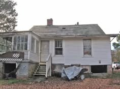 an old white house sitting in the middle of a leaf covered yard with a truck parked nearby