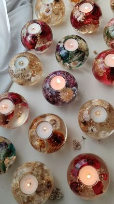 many different colored glass candles sitting on top of a white table with one lit candle in the middle