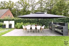 an outdoor dining area with table, chairs and grill in the middle of it is surrounded by greenery