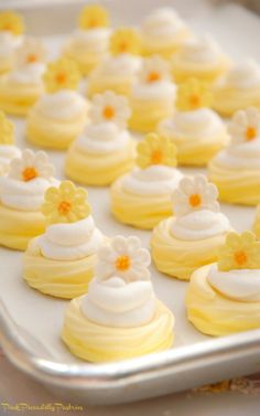 there are many small yellow and white cupcakes on the baking sheet with frosting