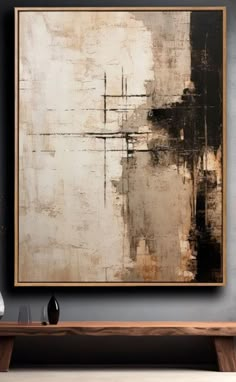 an abstract painting hangs on the wall above a wooden table in front of a gray wall