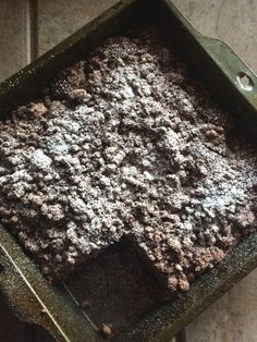 a square pan filled with brownies and powdered sugar on top of a tile floor