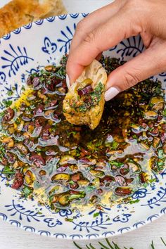 a person dipping something into a bowl of food on top of a white and blue plate