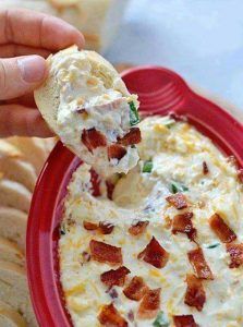 a red plate topped with bacon and cream cheese dip next to crackers on the side