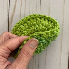 someone is crocheting a green piece of yarn on a white wooden surface with their fingers