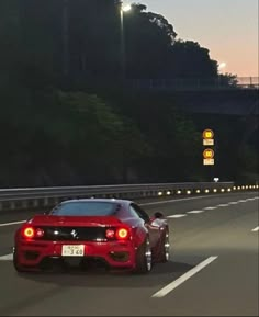 a red sports car driving down the highway at night time with its lights turned on