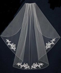 a white veil with flowers on the bottom and laces at the bottom, hanging from a black background