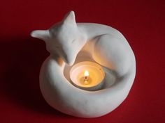 a white ceramic candle holder with a sleeping cat on it's side and a lit candle in the middle