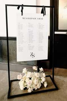 a wedding seating chart with white flowers on it and a black frame holding the table numbers