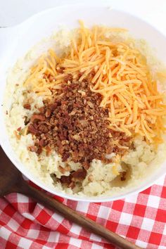 a bowl filled with mashed potatoes and cheese on top of a checkered table cloth