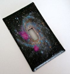 a light switch cover in the shape of a spiral galaxy with pink and blue stars