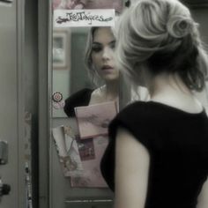 a woman standing in front of a mirror next to a door with writing on it