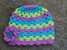 a crocheted hat with a button on the side sitting on concrete surface next to cement