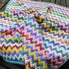 a multicolored crocheted blanket on a wooden bench