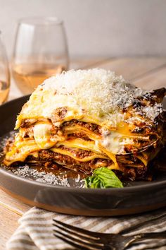 a plate with lasagna on it next to some wine glasses and napkins