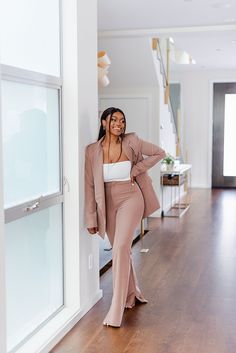 a woman leaning against a wall wearing a tan suit and white top with her hands on her hips