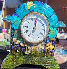 a blue clock with flowers and butterflies on it's face sitting on a table