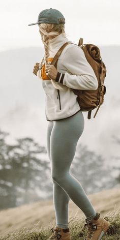 a woman in tights and boots standing on top of a grass covered hill with her back to the camera