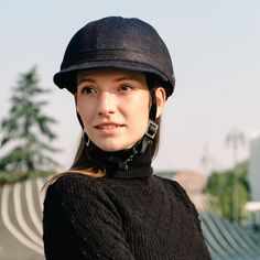 a woman wearing a black hat with ear rings on her ears and looking at the camera