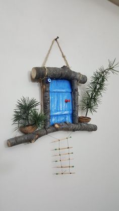 a blue door hanging from the side of a white wall next to plants and sticks