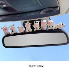 a group of toy cows sitting on top of a car mirror