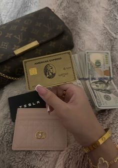 a person holding up a credit card next to other purses and money on a bed