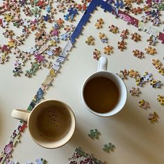 two cups of coffee sit on a table covered with puzzle pieces, which are scattered around them