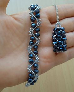 a hand is holding two bracelets with blue beads on it and silver chains hanging from them